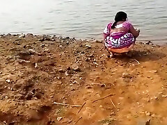 Indian girl peeing in the dirt by a lake