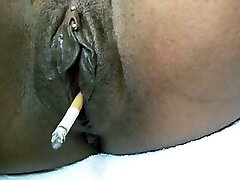 Big dark-hued shiny pussy smoking a cigarette on webcam