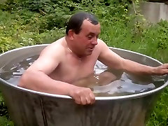 Naked old man rolls around in outside bath tub.