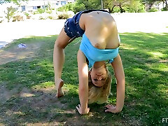 A flexible blonde girl shows her pussy in a park